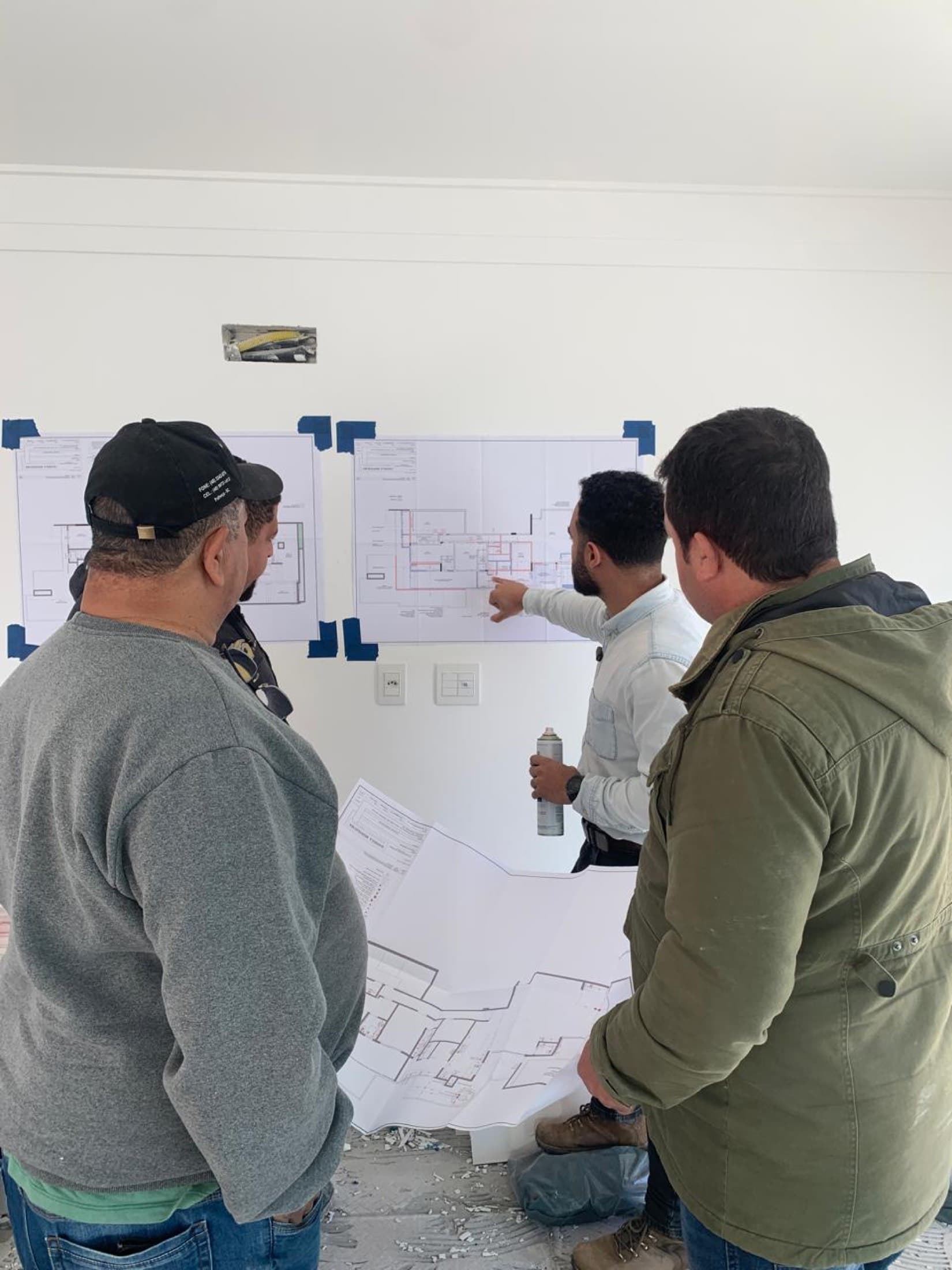 Equipe da Pronto! analisando plantas fixadas na parede durante o planejamento da obra